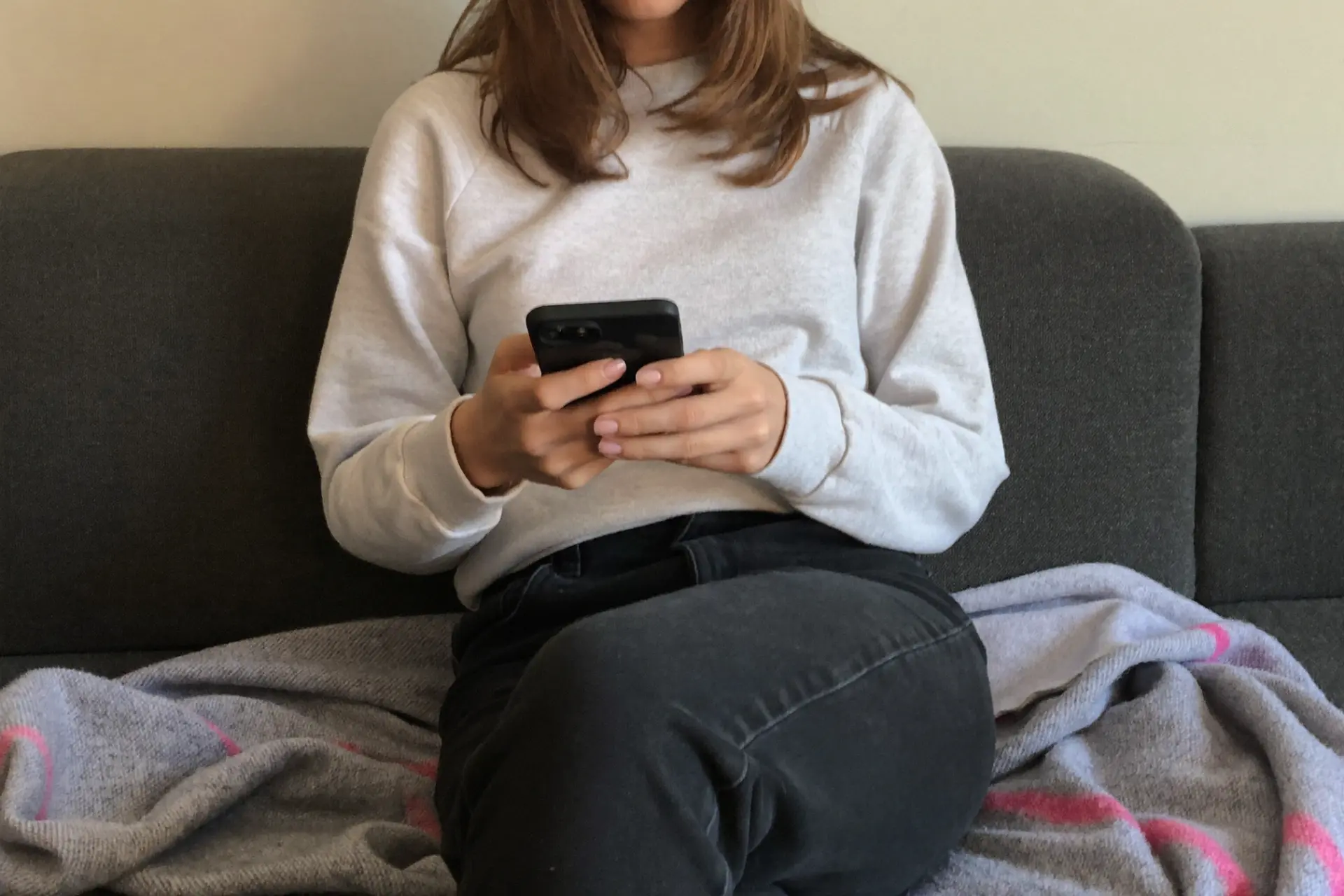 Person sitzt auf einem Sofa und tippt auf einem Smartphone